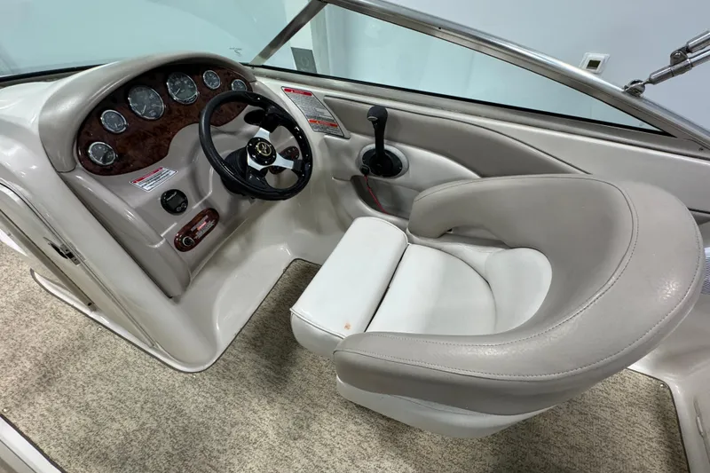 Slide: The Image of 2004 Sea Ray 200 Sundeck helm with steering wheel and gauges, featuring beige upholstery. - 13