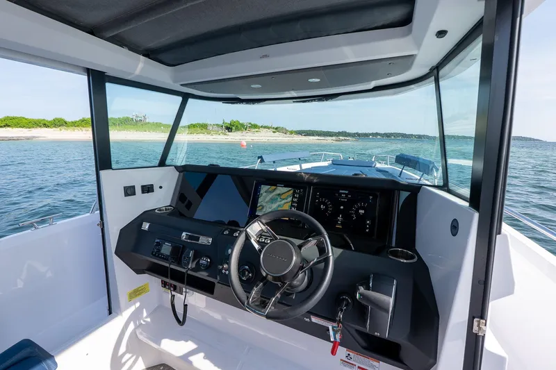 Slide: The Image of 2026 Axopar 29 Cross Cabin interior with modern dashboard and steering, overlooking scenic waters. - 18