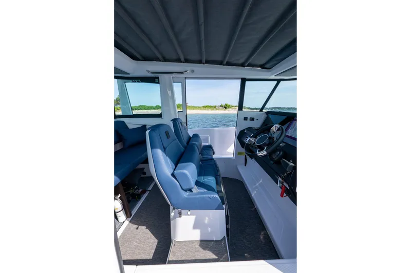 Slide: The Image of 2026 Axopar 29 Cross Cabin interior with blue seating and steering wheel, overlooking water. - 29