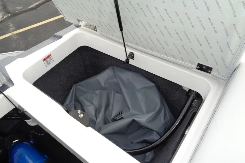 Slide: The Image of Open storage compartment in 2020 MasterCraft XT23 boat, featuring a gray cover and hydraulic support. - 10