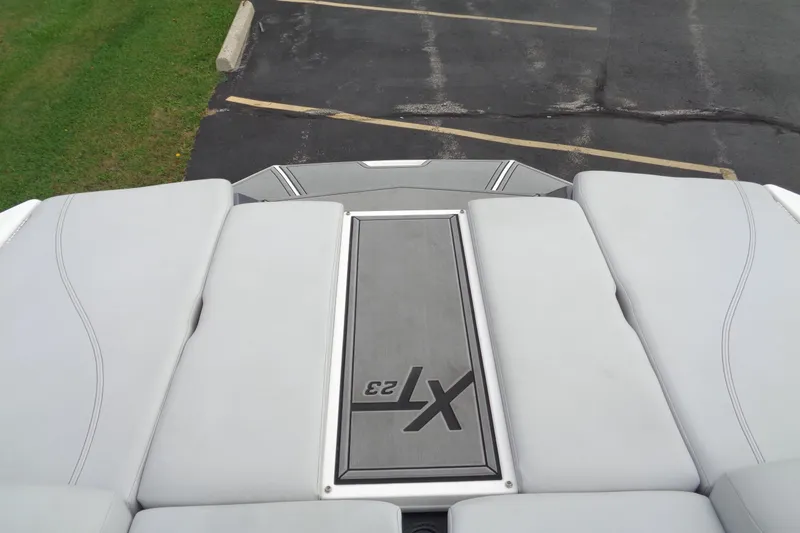 Slide: The Image of 2020 MasterCraft XT23 boat deck with cushioned seating and logo, parked on asphalt. - 11
