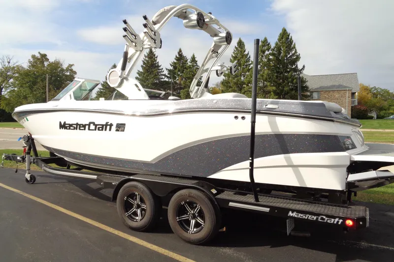 Slide: The Image of 2020 MasterCraft XT23 boat on trailer, parked outdoors, showcasing sleek design and modern features. - 2
