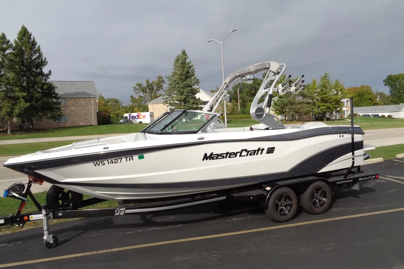 Slide: The Image of 2020 MasterCraft XT23 boat on trailer, parked outdoors near trees and buildings. - 5