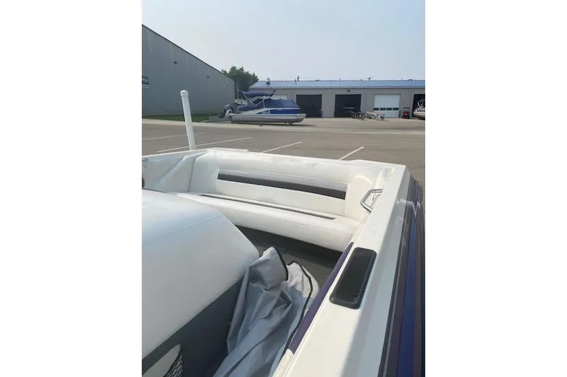 Slide: The Image of 1997 Malibu Echelon boat interior with white seating, parked near a warehouse. - 8