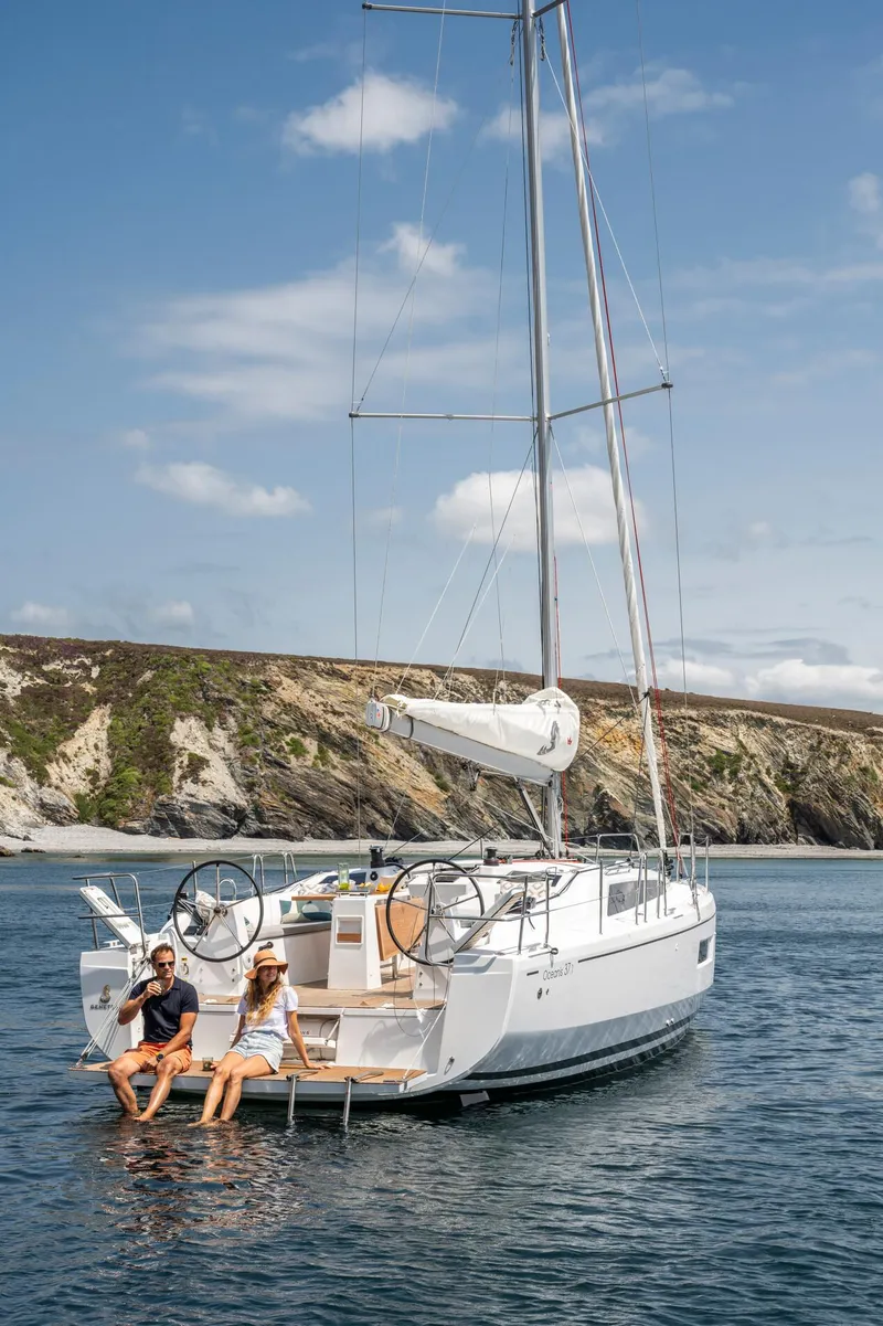 Slide: The Image of 2024 Beneteau Oceanis 37.1 sailboat anchored near rocky coastline. - 2