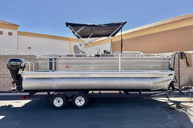 The Image of 2024 Sun Tracker Fishin' Barge 20 DLX pontoon boat on trailer, parked outdoors. - 0