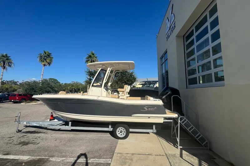 Slide: The Image of 2025 Scout 215 XSF boat on trailer, parked outside a building under clear blue sky. - 3
