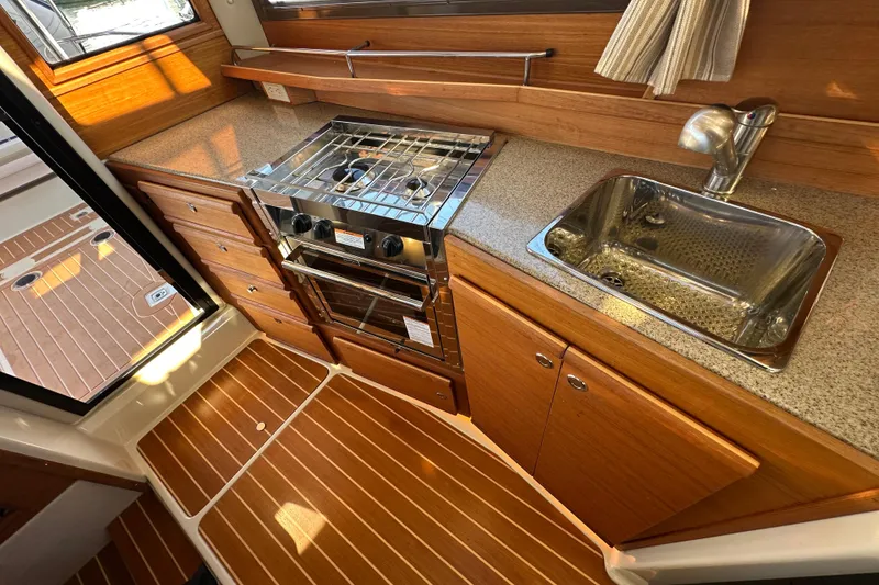 Slide: The Image of 2020 Ranger Tugs R-29 galley with stove, sink, and wood cabinetry. - 21