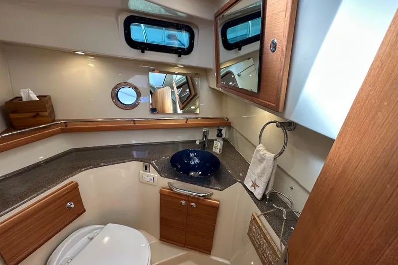 Slide: The Image of 2020 Ranger Tugs R-29 bathroom with modern fixtures, wooden cabinetry, and a porthole window. - 34