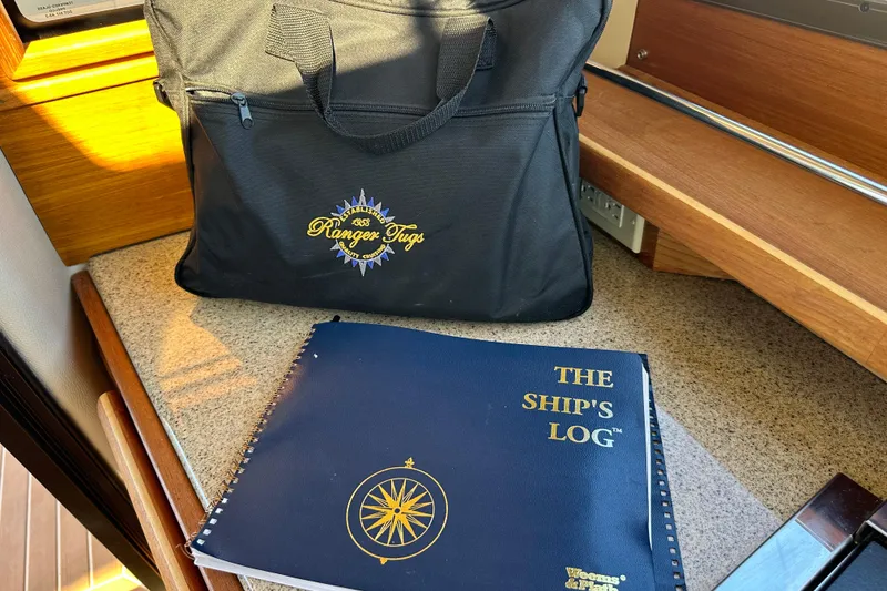 Slide: The Image of Black Ranger Tugs bag and ship's logbook on a wooden boat interior surface. - 37