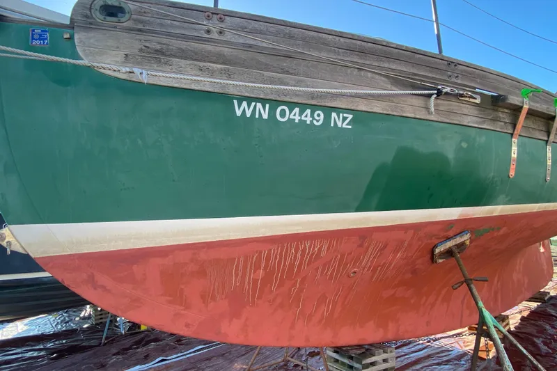 Slide: The Image of 1978 Bristol Channel Cutter 28 sailboat with green and red hull, docked on land. - 2