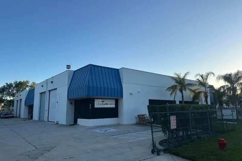 Slide: The Image of Exterior view of East Marine Boats facility with palm trees and blue awnings. - 11