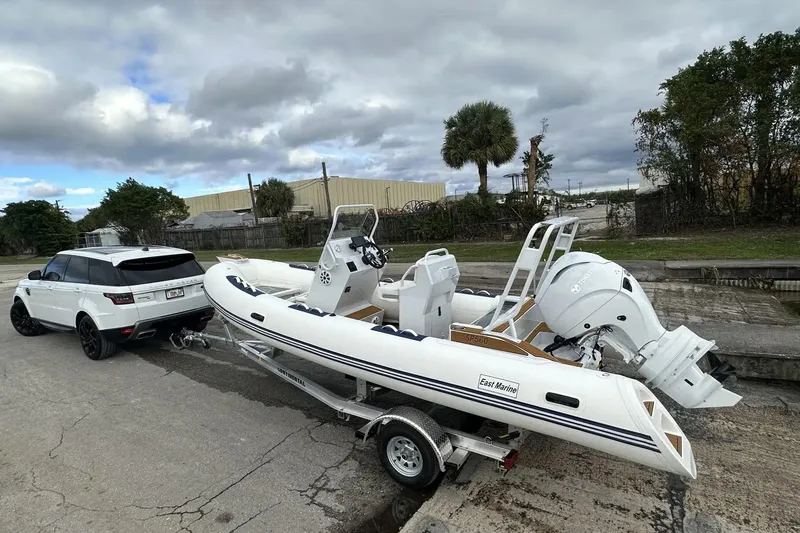 Slide: The Image of White East Marine 560 boat on trailer, hitched to a white SUV, outdoors. - 13
