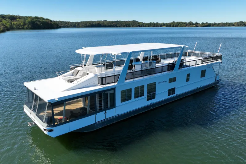 The Image of 2013 Thoroughbred 80'x 18' houseboat on a serene lake under clear skies. - 0