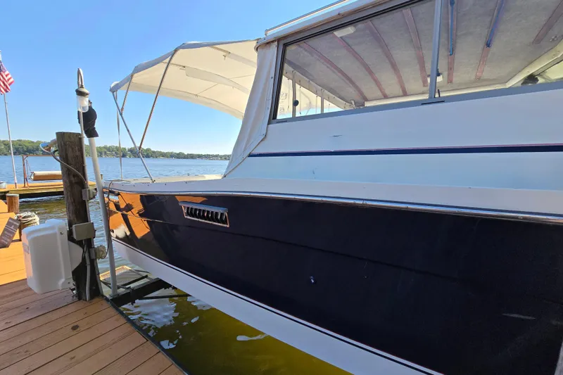 Slide: The Image of 1984 Bayliner 2802 Trophy boat docked by a serene lake under clear blue skies. - 6