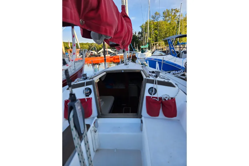 Slide: The Image of 1981 Catalina Capri 25 sailboat docked, featuring red sail cover and open cabin entrance. - 5