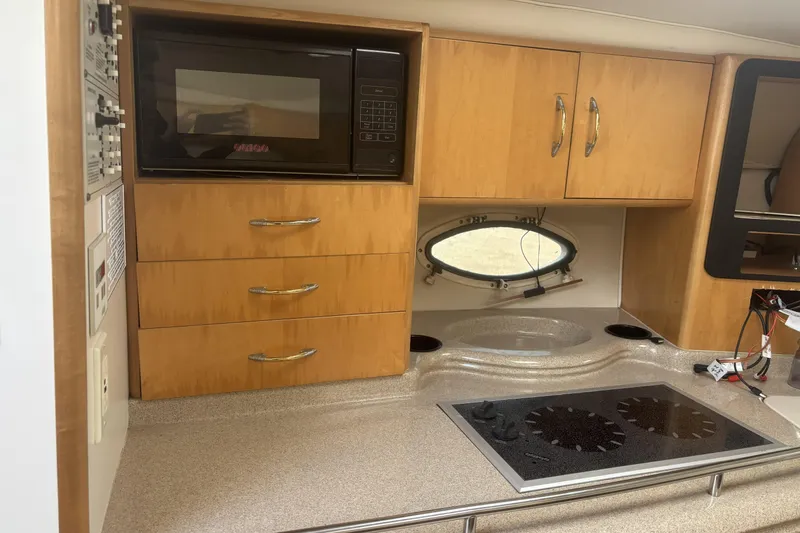 Slide: The Image of 2000 Larson Cabrio 330 Mid Cabin kitchen with microwave, stove, and wooden cabinets. - 24