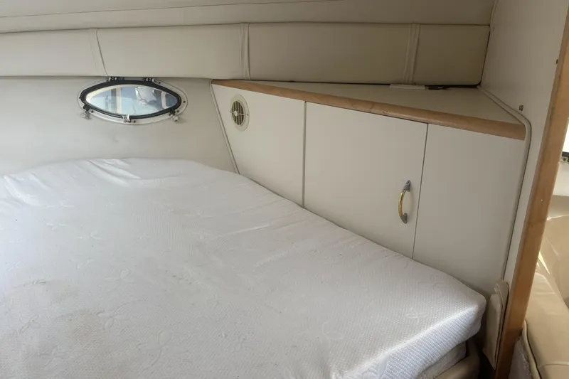 Slide: The Image of 2000 Larson Cabrio 330 Mid Cabin interior with bed, porthole, and storage cabinets. - 28