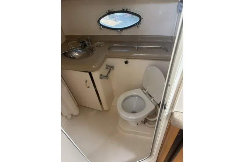 Slide: The Image of 2000 Larson Cabrio 330 Mid Cabin bathroom with sink, toilet, and porthole window. - 33