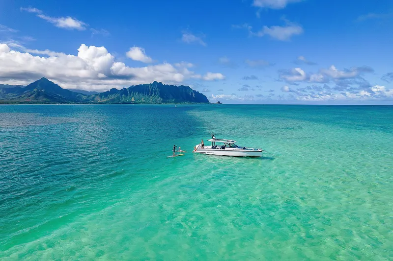 Slide: The Image of 2021 Axopar Suntop Brabus Trim in turquoise waters, with paddleboarders and scenic mountains. - 2