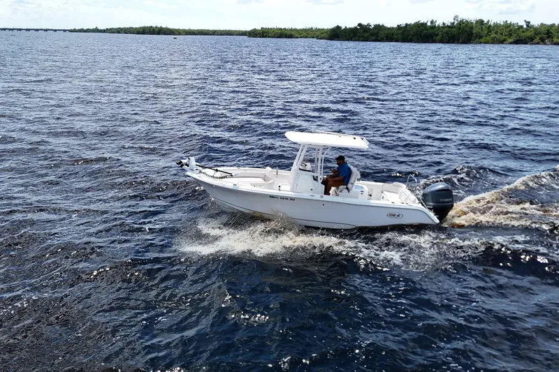 Slide: The Image of 2021 Sea Hunt Ultra 234 boat cruising on open water, with lush greenery in the background. - 27