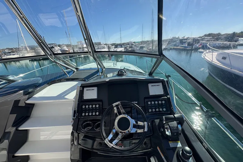 Slide: The Image of 2018 Monterey 335 Sport Yacht helm with marina view, showcasing controls and steering wheel. - 10