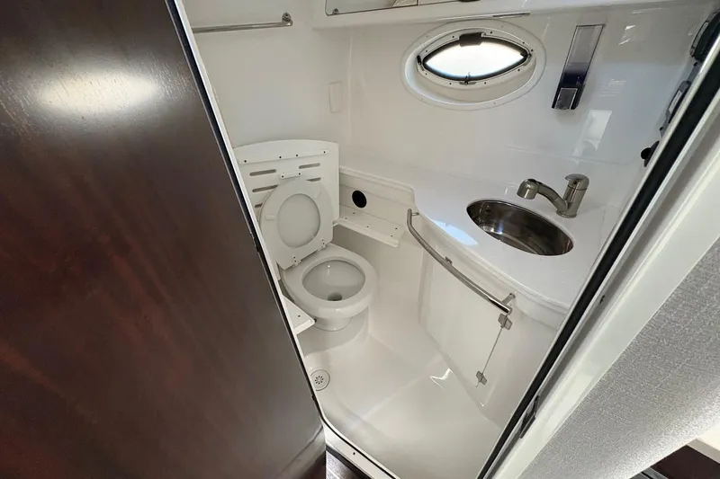 Slide: The Image of 2018 Monterey 335 Sport Yacht bathroom with toilet, sink, and porthole window. - 21