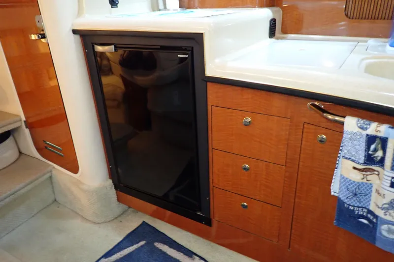 Slide: The Image of 2002 Sea Ray 340 Sundancer interior kitchen with fridge, wooden cabinets, and sink. - 79