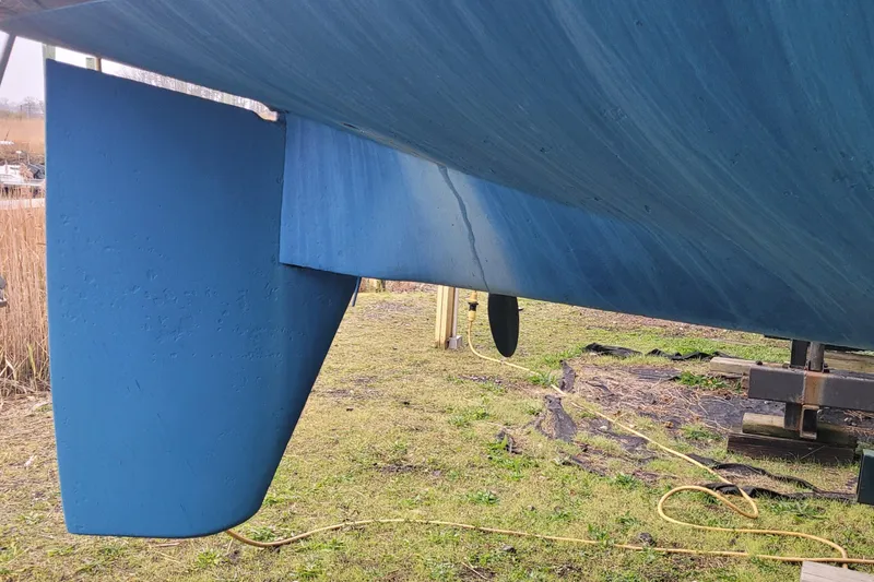 Slide: The Image of 1986 Sabre 34 sailboat keel and rudder, blue hull, on land. - 18