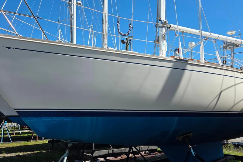 Slide: The Image of 1986 Sabre 34 sailboat on land, white hull with blue stripe, clear sky background. - 30