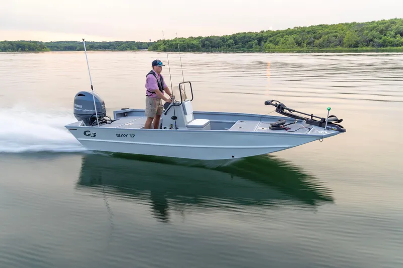 The Image of 2026 G3 Bay 17 boat cruising on a calm lake with lush green shoreline. - 0