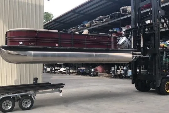 Slide: The Image of 2018 Coach Pontoons 24 Tri-toon being lifted by a forklift in a storage facility. - 1