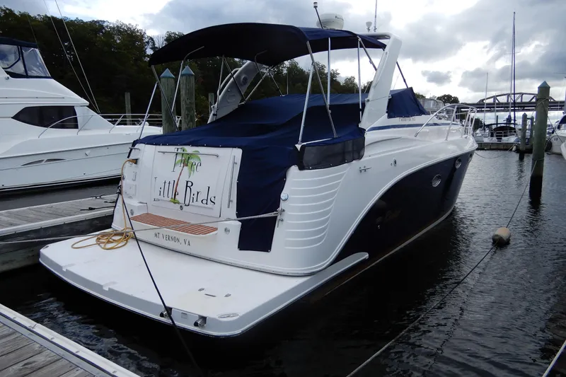 Slide: The Image of 2005 Rinker 360 Express Cruiser docked, rear view with blue cover, named "Three Little Birds." - 2