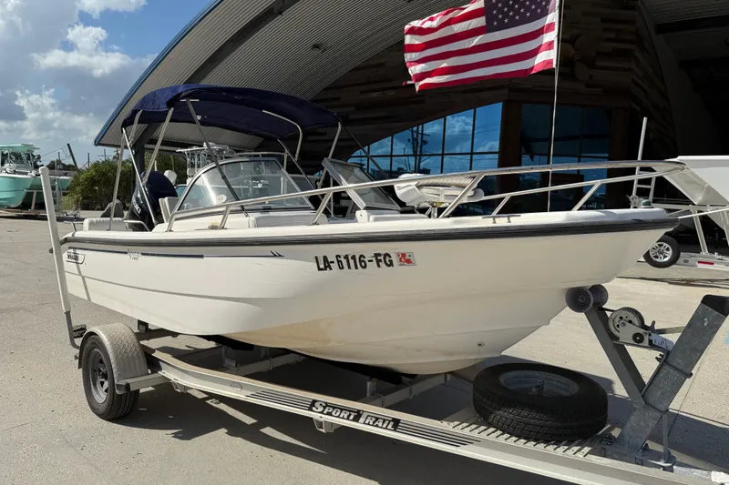 Slide: The Image of 2002 Boston Whaler Ventura 160 boat on trailer with American flag, parked outdoors. - 2
