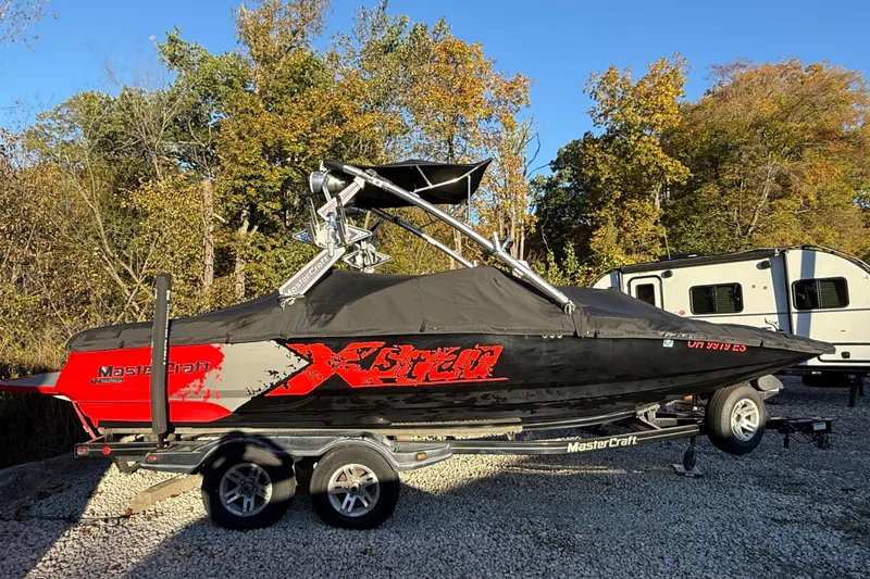 The Image of 2008 MasterCraft XStar 23 boat on trailer, covered, with autumn trees in background. - 1
