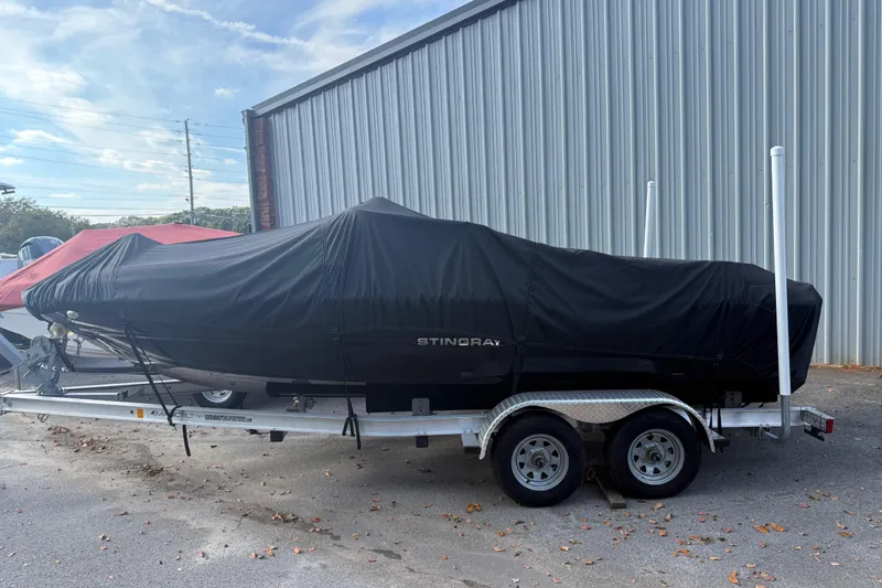Slide: The Image of 2019 Stingray 198 LX boat covered on trailer near metal building. - 52