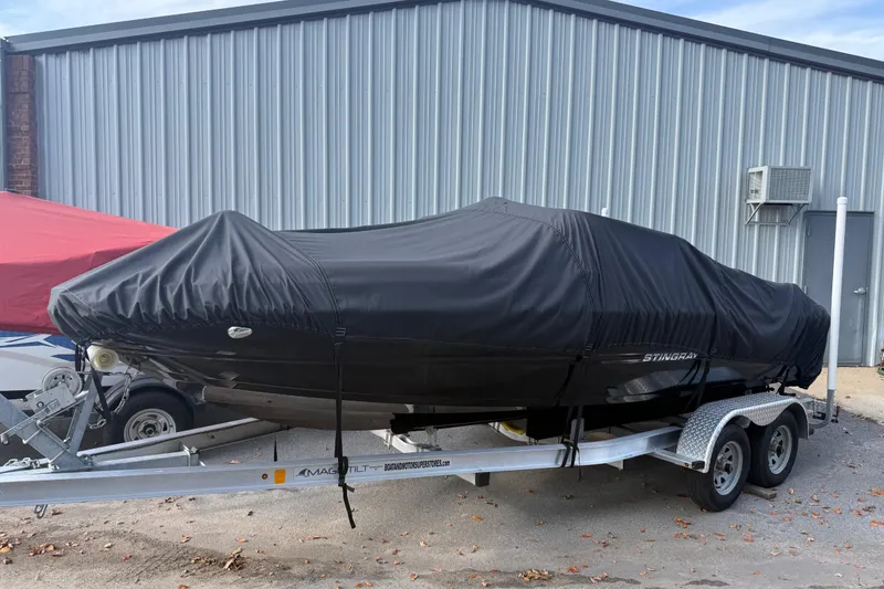Slide: The Image of 2019 Stingray 198 LX boat covered on trailer, parked by metal building. - 53