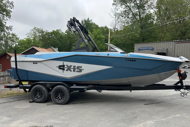 Slide: The Image of 2025 Axis T220 boat on trailer, blue and white design, parked outdoors. - 2