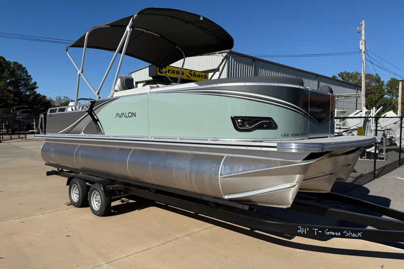 The Image of 2026 Avalon LSZ Versatile Rear Bench pontoon boat on trailer, parked outdoors. - 0
