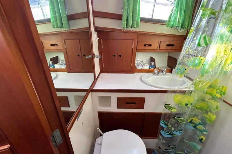 Slide: The Image of 1986 Grand Banks 42 Classic yacht bathroom with wooden cabinets and fish-themed shower curtain. - 49