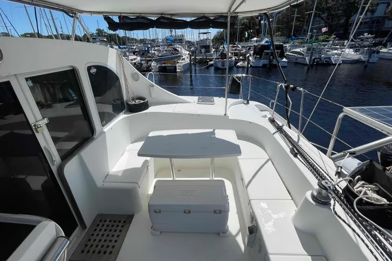 Slide: The Image of 2003 Lagoon 410-S2 catamaran cockpit with seating, table, and helm, docked by the water. - 69
