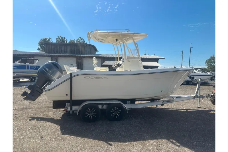 Slide: The Image of 2023 Cobia 220 Center Console boat on trailer, parked outdoors under clear blue sky. - 15