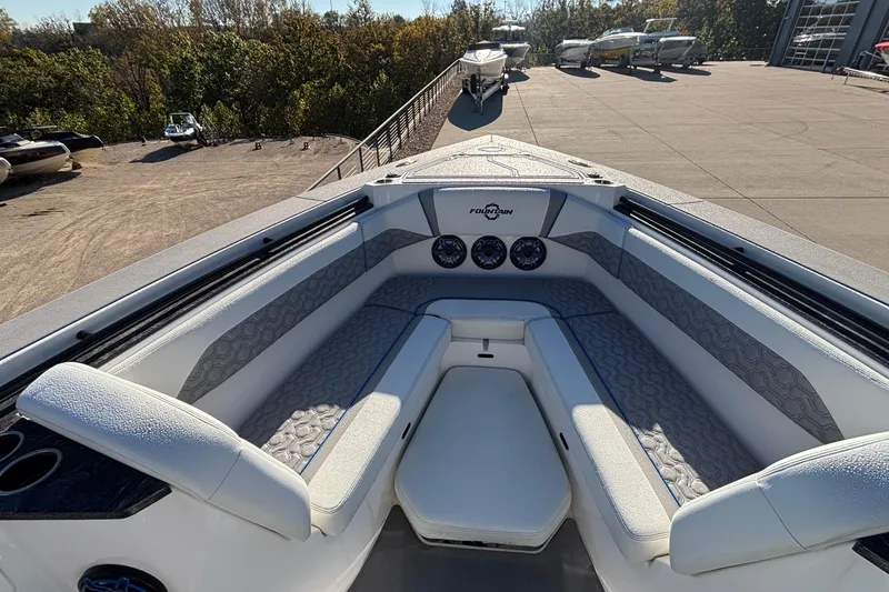 Slide: The Image of 2024 Fountain 38 SCX boat interior with cushioned seating and dashboard, parked outdoors. - 14