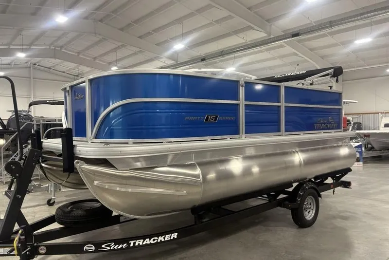 Slide: The Image of 2026 Sun Tracker Party Barge 16 DLX pontoon boat in showroom, blue and silver design. - 6