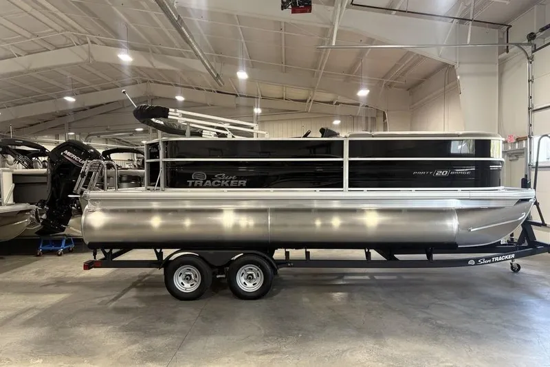 The Image of 2026 Sun Tracker PARTY BARGE® 20 DLX pontoon boat on trailer in a showroom. - 0