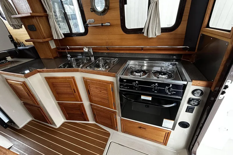 Slide: The Image of 2015 Ranger Tugs R-31 CB galley with stove, sink, and wooden cabinetry. - 9