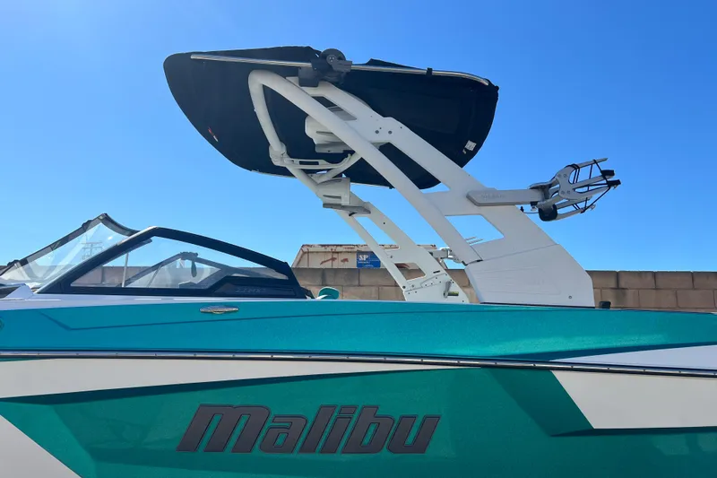 Slide: The Image of 2020 Malibu Wakesetter 23 MXZ boat with teal and white design under clear blue sky. - 20