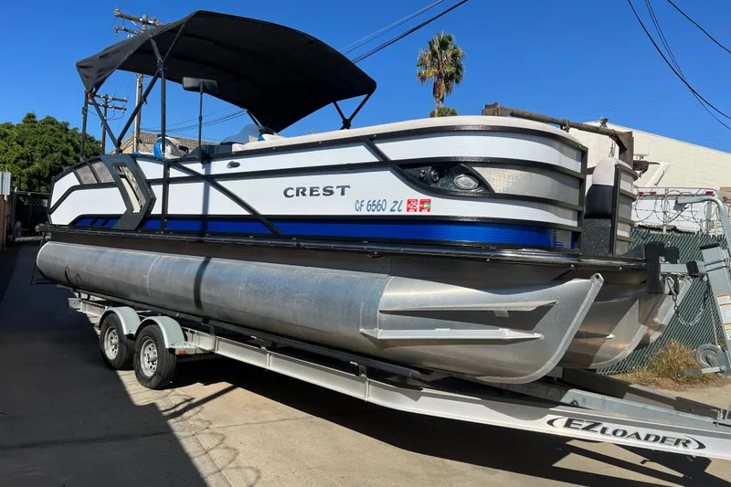 Slide: The Image of 2020 Crest Caribbean RS 250 SLRC pontoon boat on trailer, parked outdoors. - 2