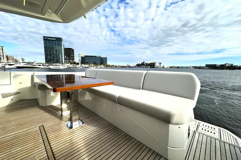 Slide: The Image of 2023 Prestige 590 yacht deck with seating, table, and waterfront cityscape view. - 10
