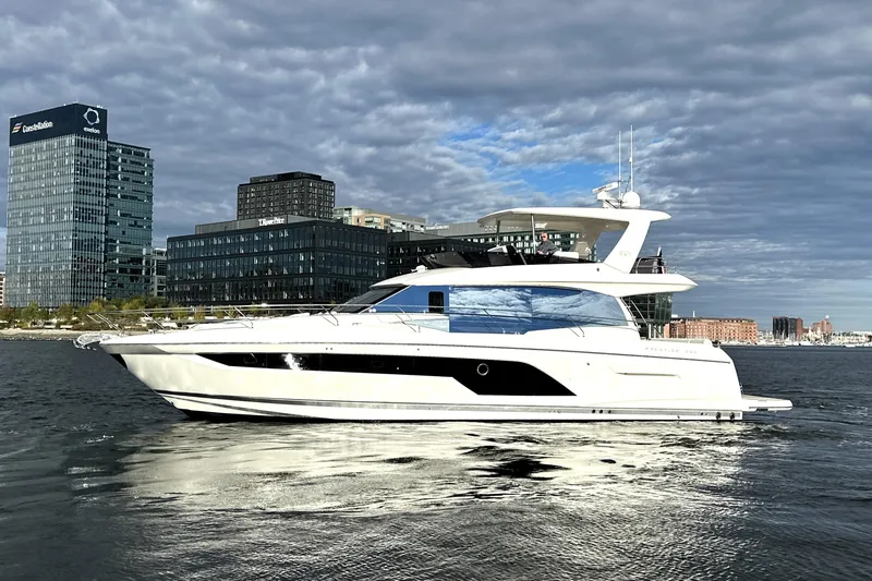 Slide: The Image of 2023 Prestige 590 yacht cruising near modern city skyline under cloudy sky. - 5